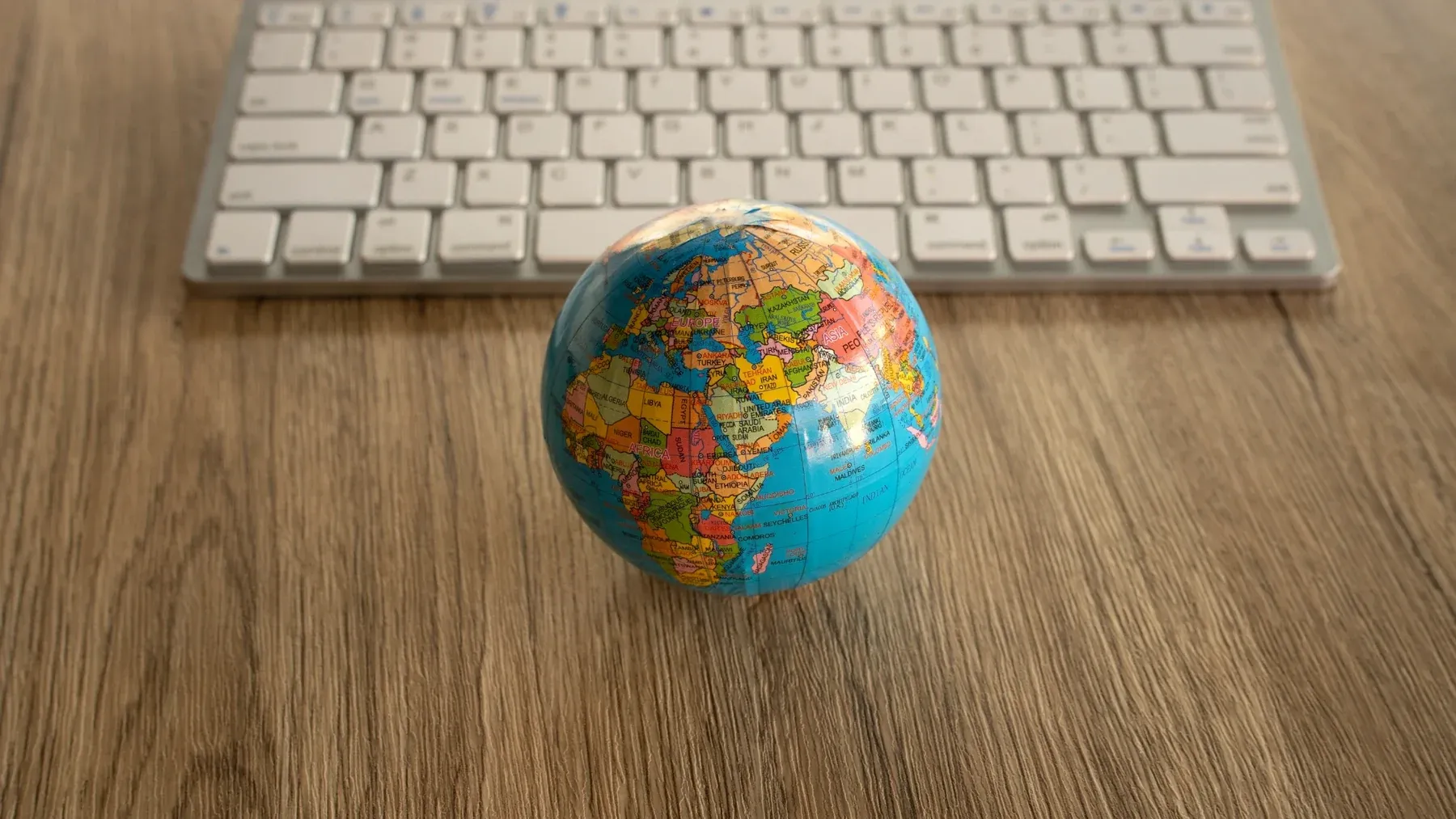 A small desk globe on a wooden desk beside a keyboard.
